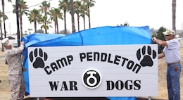 Staff Sgt. Andrew Reid, the canine chief with the Camp Pendleton Marine Corps Police Department, and Jon Hemp, the co-founder of The Dawgs Project, unveil the Camp Pendleton War Dogs sign here July 20. The sign was made by Sgt. Adam L. Cann before he was killed in action by a suicide-bomb attack on an Iraqi police recruitment center.