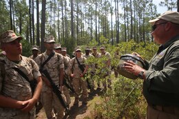 Marines from Combat Logistics Battalion 2, 2nd Marine Logistics Group, listen as counter-IED instructor Travis Hillertalks about a mock IED made from a pressure cooker, planted by instructors on an IED training path in Holly Ridge, North Carolina, August 19, 2014.  Instructors hid several mock IED's to test the group's ability to spot the fake bombs while on a foot-patrol.  Earlier that day, the Marines received classroom instruction about various visual indicators in identifying IED's.