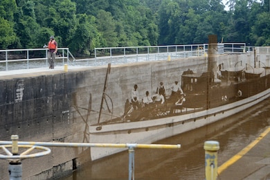 Civil Engineer Chris Norton looks for discrepencies atop the lock chamber during the annual inspection of Lock and Dam 1 on the Cape Fear River. Superimposed is an image of the steamer Mercur that passed through the locks in July of 1915. The locks are still used by recreational boaters to make their way down river. (USACE photo by Hank Heusinkveld)